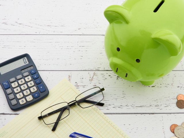 A green piggy bank beside a calculator, notepad and coins